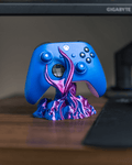 Skullflame Controller-Halter mit blauem Gaming-Controller, auf Holz-Schreibtisch mit Mauspad, im Hintergrund ein Gaming-Monitor mit Spielszene.