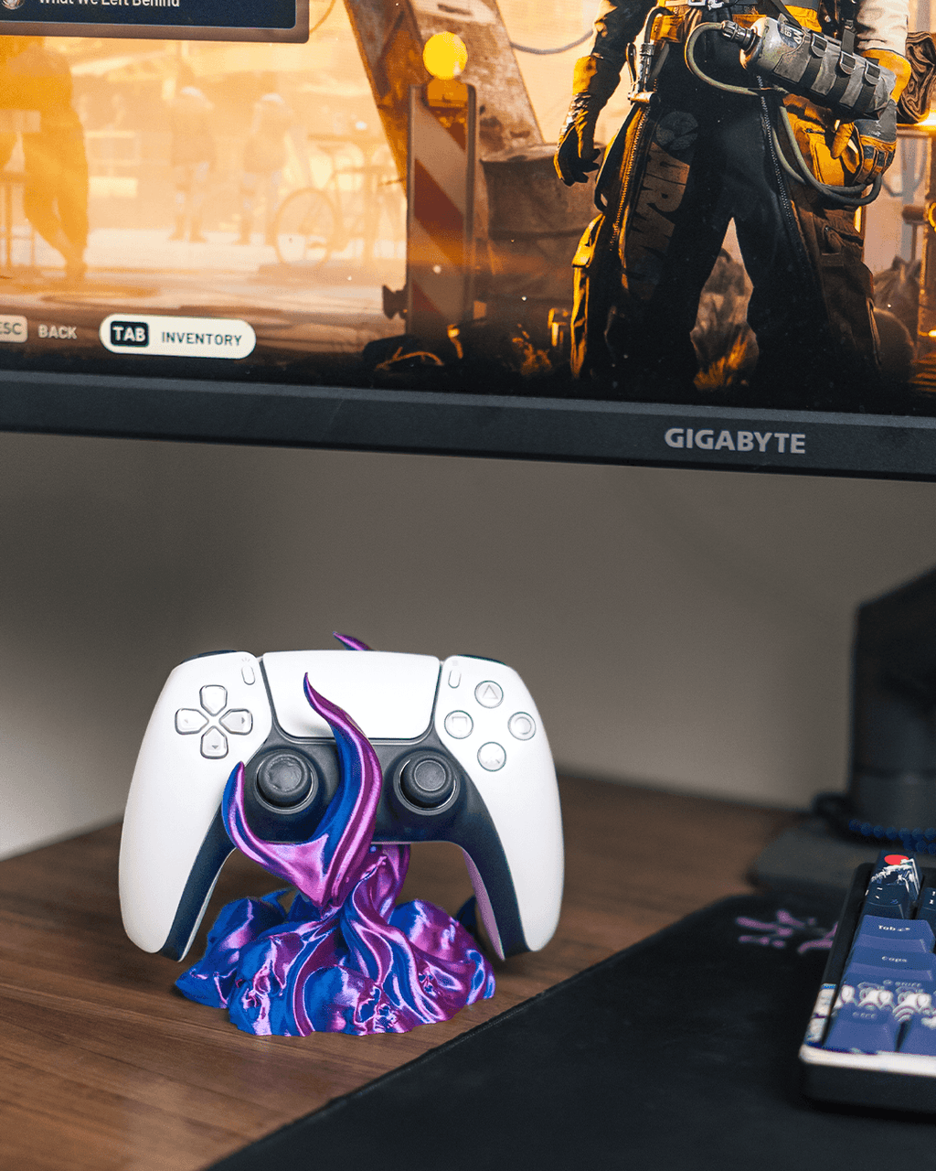 Skullflame Controller-Halter mit weißem Gaming-Controller, auf Holz-Schreibtisch, im Hintergrund ein Gaming-Monitor mit Spielszene und Tastatur.
