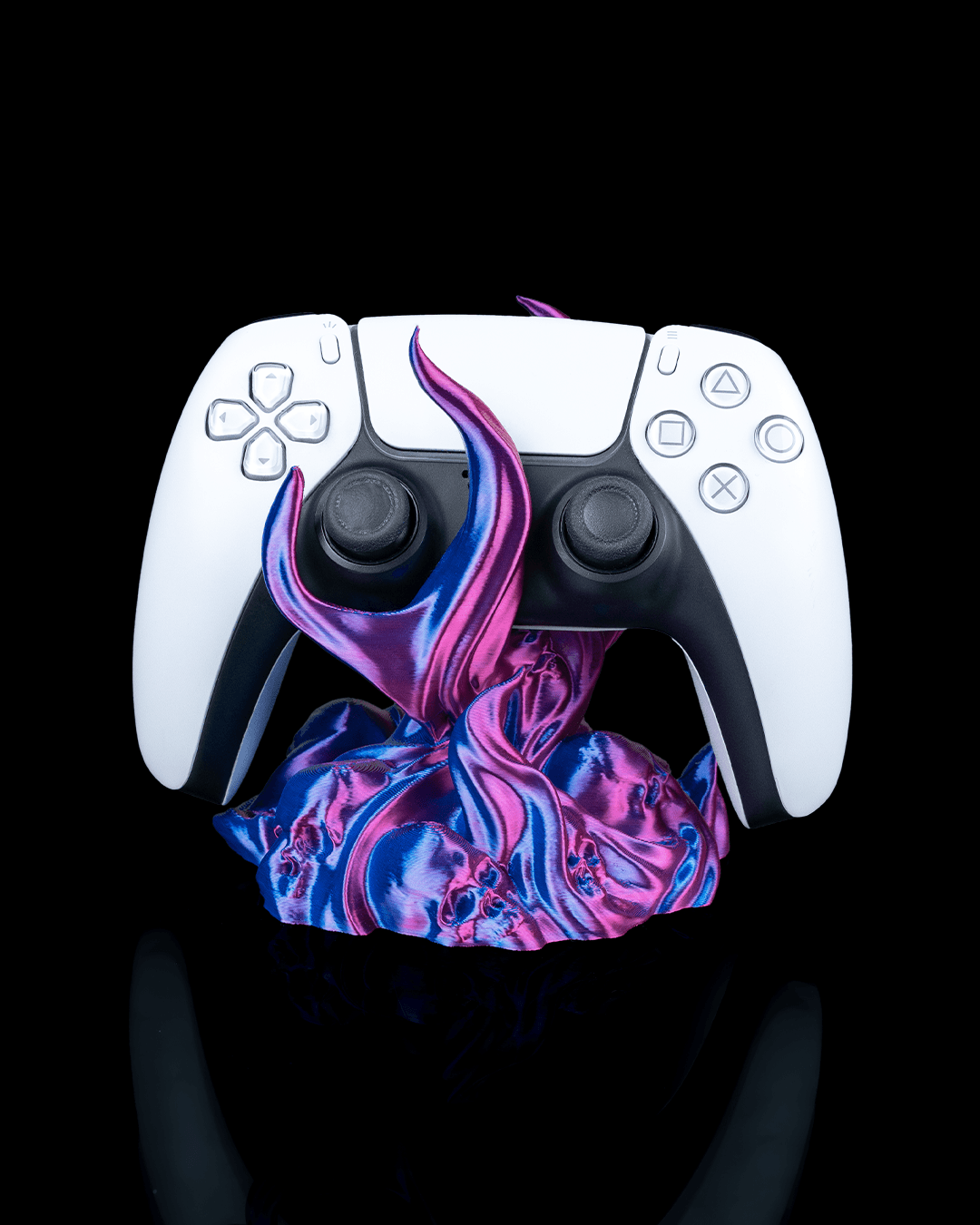 Skullflame Controller-Halter mit weißem Gaming-Controller, Frontalansicht freigestellt vor schwarzem Hintergrund, Totenkopf-Reliefs im pink-lila-blauen Sockel sichtbar.