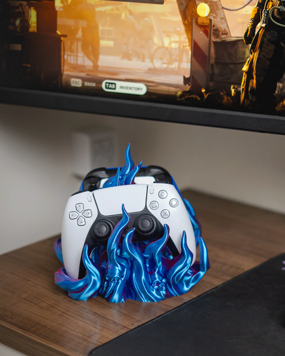 Skullflame Dual Controller-Halter in Blau, Lifestyle-Foto auf Schreibtisch mit weißem und dunkelblauem Gaming-Controller nebeneinander, im Hintergrund ein Monitor mit Spielszene.