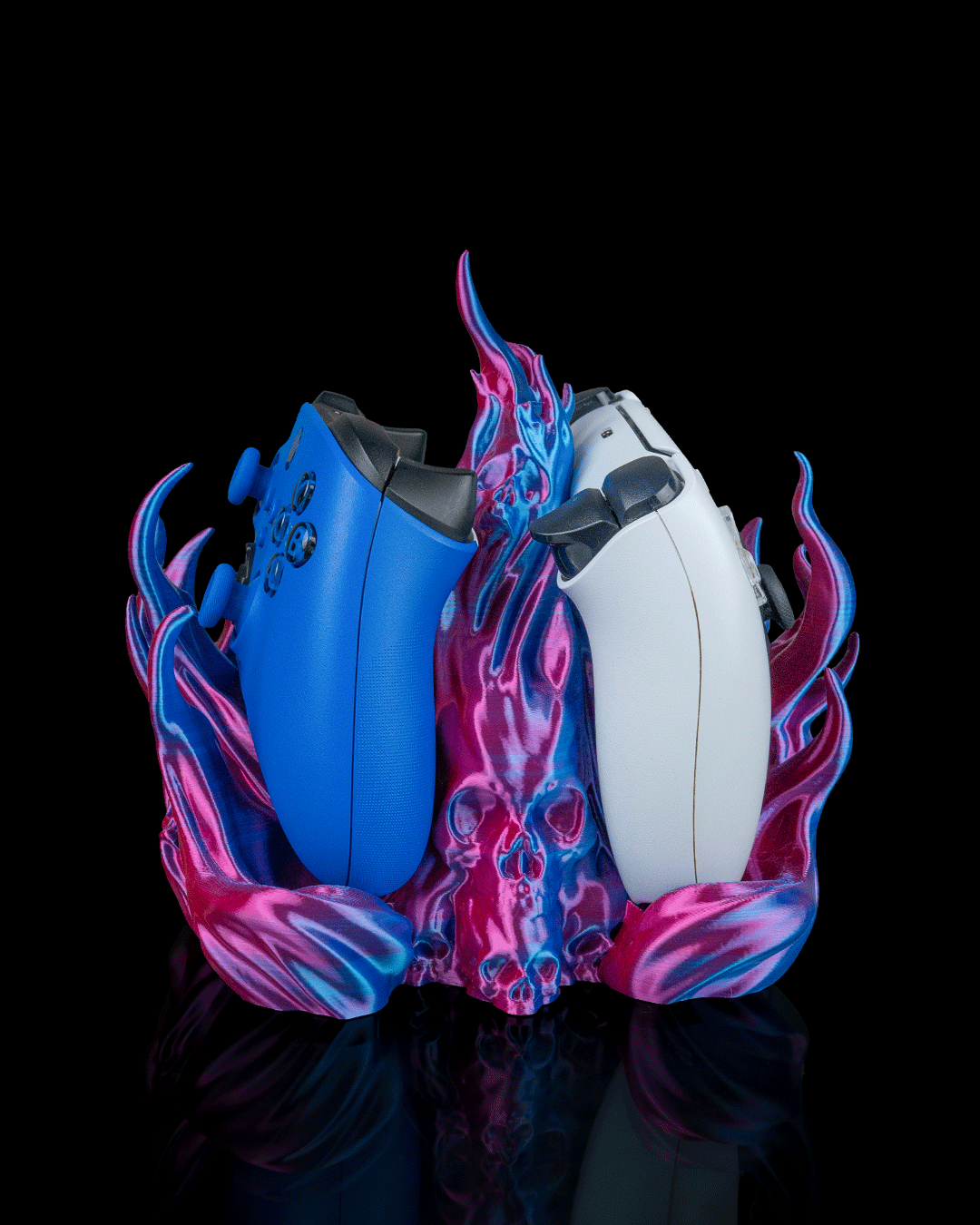 Skullflame Dual Controller-Halter in Pink-Blau, Seitenansicht freigestellt vor schwarzem Hintergrund, blauer und weißer Gaming-Controller nebeneinander mit Totenkopf-Relief mittig im Sockel.
