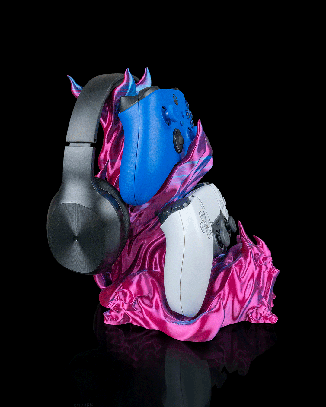 Skullflame Headset & Controller Ständer in Pink-Lila, Ansicht schräg von der Seite freigestellt vor schwarzem Hintergrund, mit hängendem Over-Ear-Kopfhörer sowie blauem und weißem Gaming-Controller.