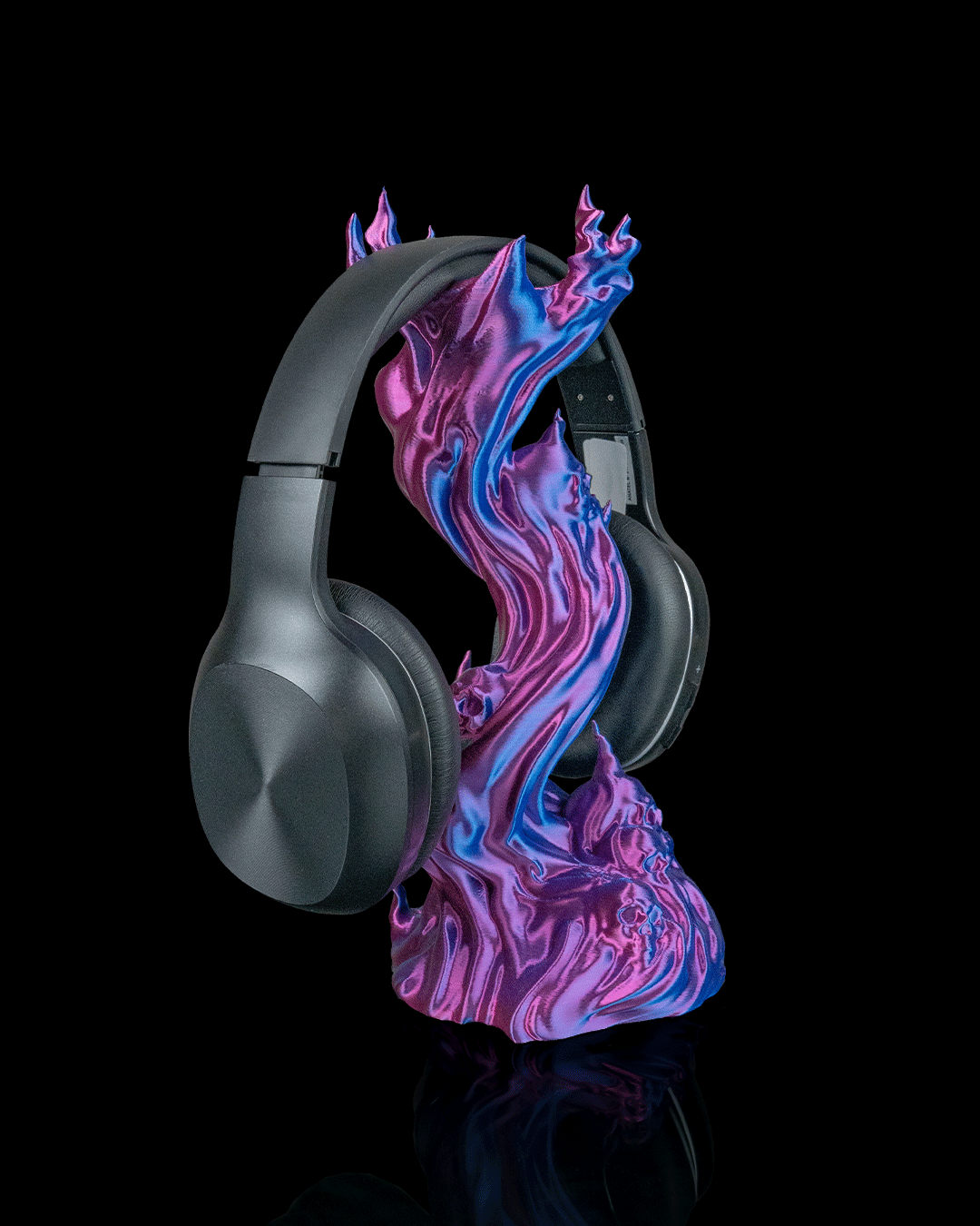 Skullflame Headset-Halter in Blau-Lila, Ansicht schräg von der Seite mit aufgehängtem Over-Ear-Kopfhörer, mehrere Totenkopf-Reliefs im unteren Sockel sichtbar, freigestellt vor schwarzem Hintergrund.