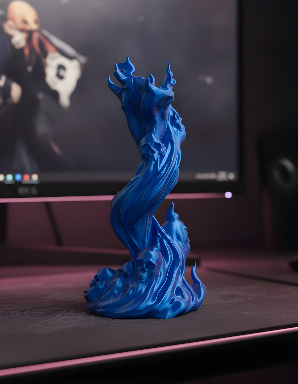 Skullflame Sockel in Blau ohne Kopfhörer, seitliche Ansicht mit sichtbaren Totenkopf-Reliefs im Sockel, auf dunklem Gaming-Schreibtisch vor einem Monitor mit pinkfarbenem Spielgeschehen.