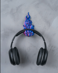 Skullflame Wand-Headset-Halter in Blau-Pink mit aufgehängtem Over-Ear-Kopfhörer, Frontalansicht an heller marmorierter Wand, Totenkopf-Reliefs im Flammen-Sockel sichtbar.