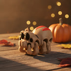 Chibi-Spinnen-Figur aus 3D-Druck in Nahaufnahme mit großen Kulleraugen und acht ausgestellten Beinchen auf Holztisch, Kürbis und Herbstlaub im Hintergrund.