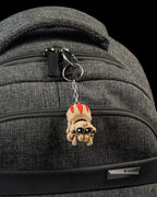 Spinnen-Schlüsselanhänger hängt kopfüber am Reißverschluss eines grauen Rucksacks, befestigt mit Metallring und Kette.