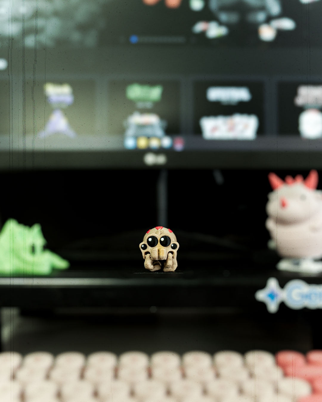 Kleine Spinnen-Figur steht auf einem Gaming-Schreibtisch vor einem Monitor, umgeben von weiteren Mini-Sammelfiguren.