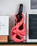 Tänzerin-Weinflaschenhalter in Pink auf Sideboard mit Bilderrahmen im Hintergrund, Frontalansicht mit Weinflasche – Münch3D