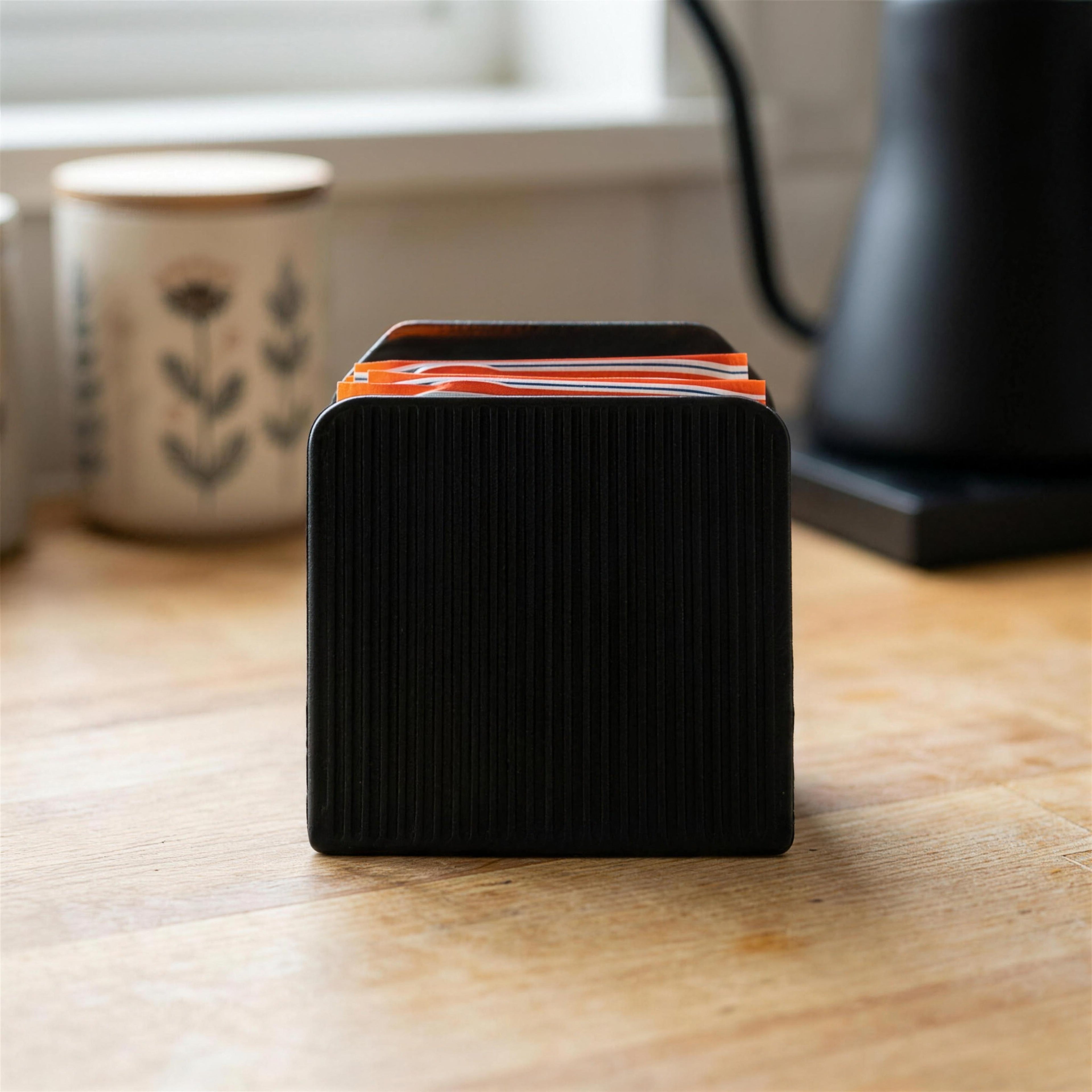 Front view of the ribbed back wall on the black Tea Cascade tea bag dispenser with all four slots filled