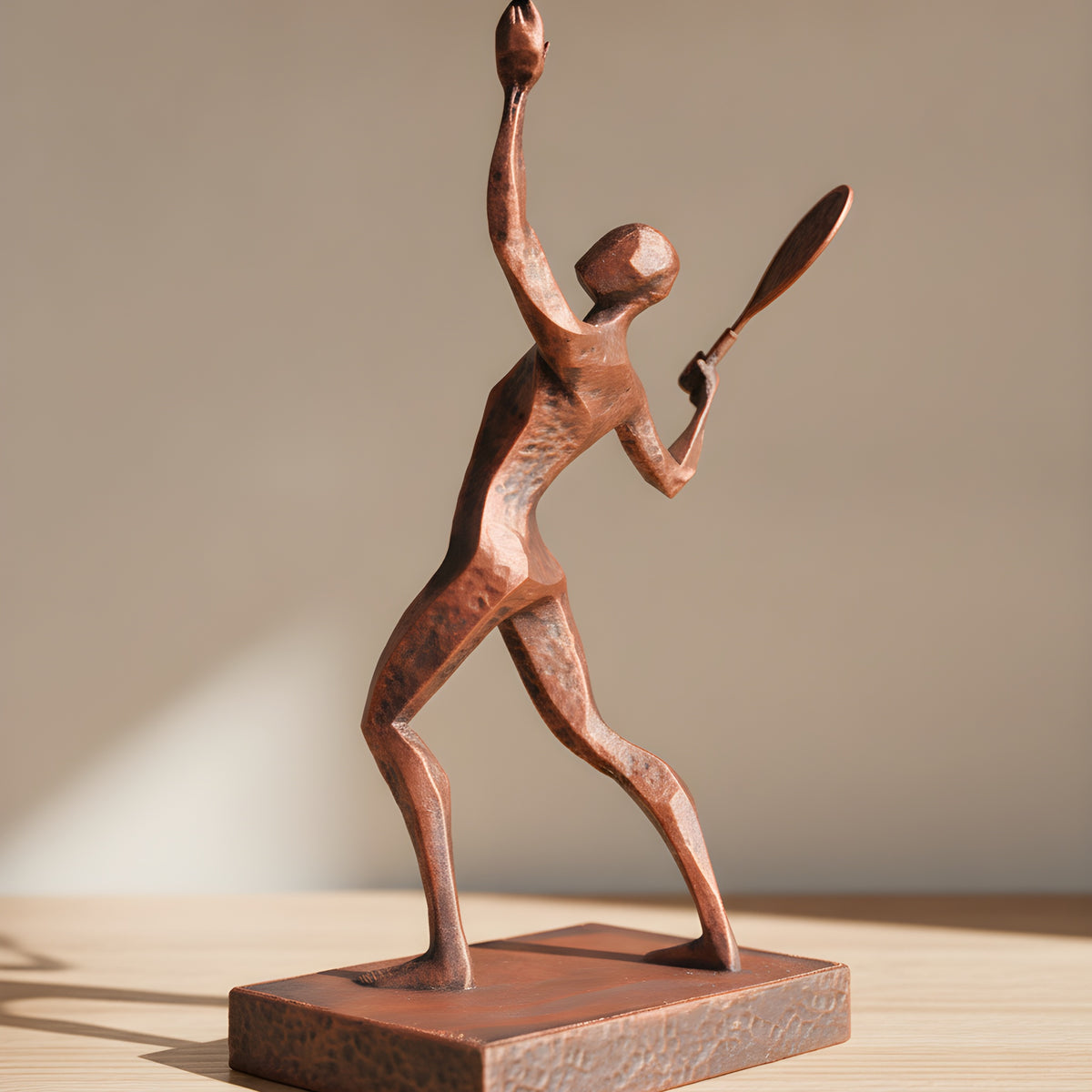 Tennisspieler-Statue in Kupfer-Bronze-Optik, Seitenansicht der Aufschlagpose mit Schläger und Ball auf Holzoberfläche, weich unscharfer warmer Hintergrund – Münch3D