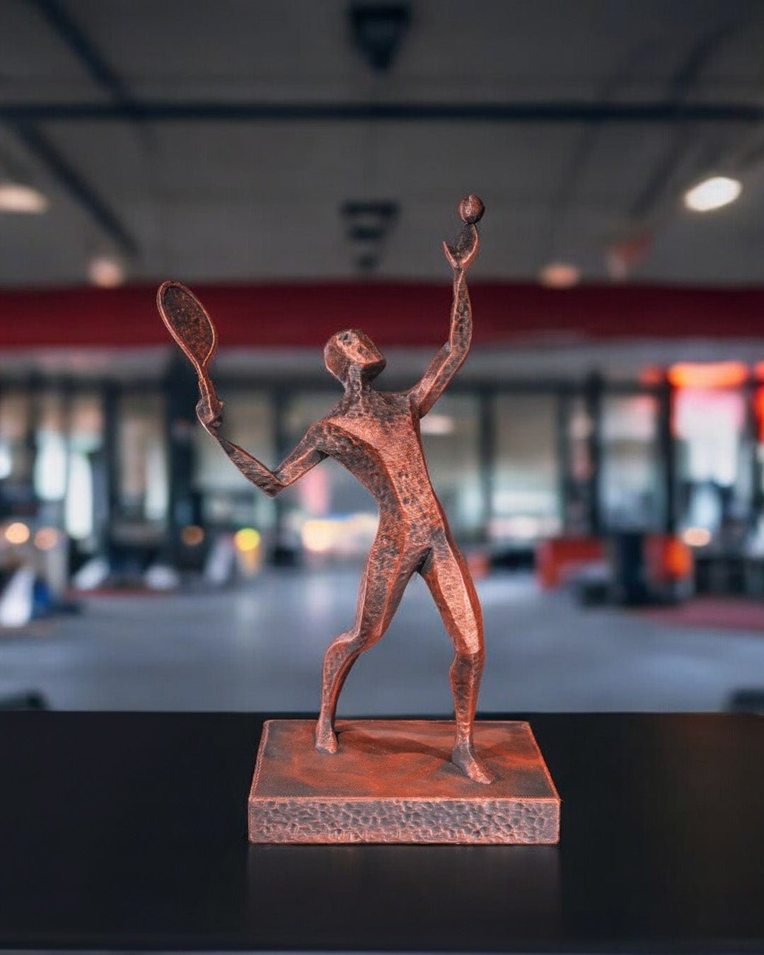 Tennis Statue handbemalt in Kupfer-Bronze-Optik, Aufschlagpose mit Schläger und Ball – Lifestyle-Aufnahme in einer Sporthalle
