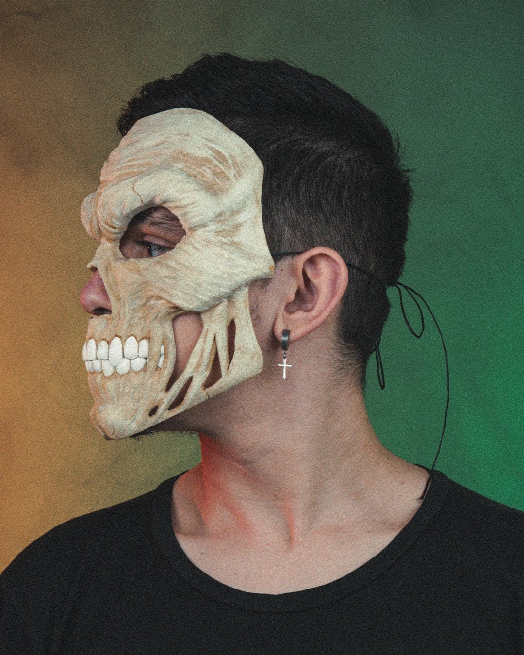 Totenkopf-Halloween-Maske in Creme getragen von einer Person, Seitenprofil mit Ohrring sichtbar, bunter Farbverlauf-Hintergrund