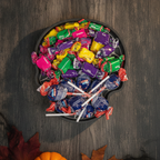 Totenkopf-Schale mit Spinnennetz-Muster von oben, gefüllt mit bunt verpackten Bonbons und Lollis, Halloween-Tischdeko mit Kürbis und Herbstlaub