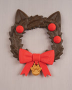 Weihnachtskranz in Katzenkopf-Form mit Katzenohren, roten Kugeln, roter Schleife und goldenem Pfotenanhänger, Frontalansicht an heller grauer Wand