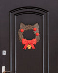Weihnachtskranz in Katzenkopf-Form mit Katzenohren, roten Kugeln, roter Schleife und goldenem Pfotenanhänger, an dunkler Zimmertür mit Türgriff und Schloss montiert