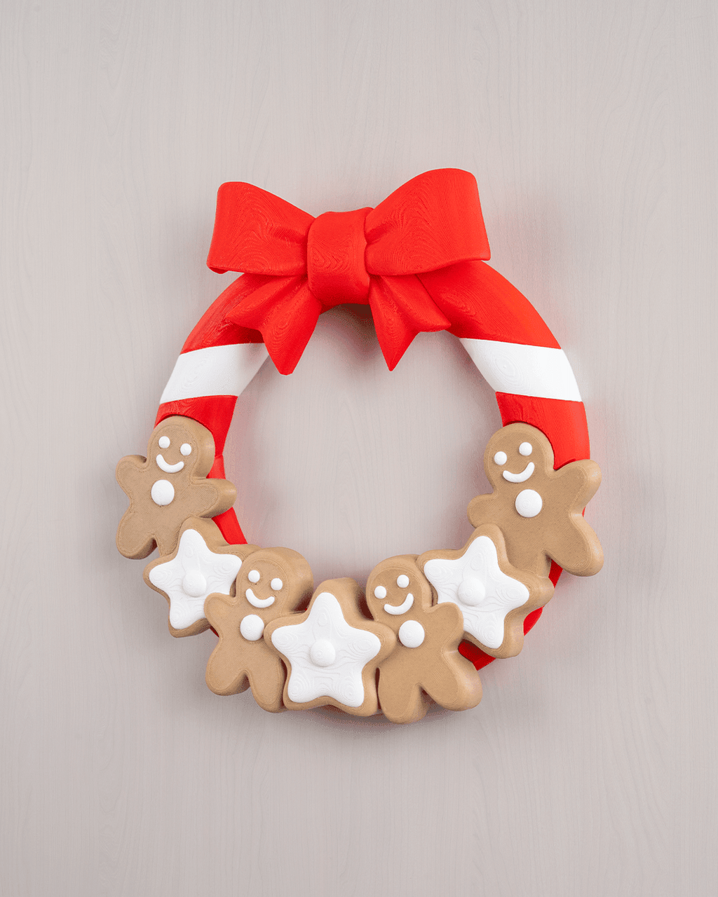 Weihnachtstürkranz mit Lebkuchenmännern, weißen Sternen und roter Schleife, Frontalansicht an heller grauer Holzwand