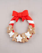 Weihnachtstürkranz mit Lebkuchenmännern, weißen Sternen und roter Schleife, Frontalansicht an heller grauer Holzwand