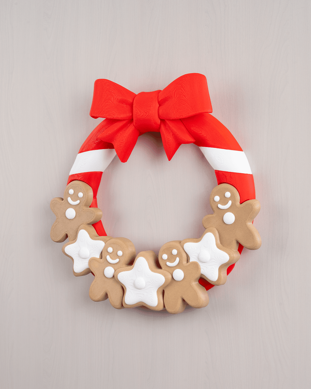 Weihnachtstürkranz mit Lebkuchenmännern, weißen Sternen und roter Schleife, Frontalansicht an heller grauer Holzwand