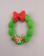 Weihnachtskranz aus grüner Strickoptik mit rotem Schleifen-Band und Rentier-Applikation mit roter Nase, Frontalansicht an heller grauer Wand