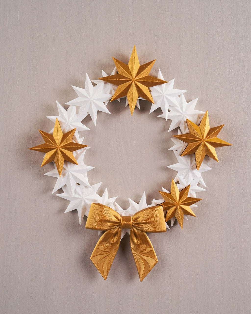 Sternenkranz aus weißen und goldenen 3D-gedruckten Sternen mit goldener Schleife, Frontalansicht an heller Wand