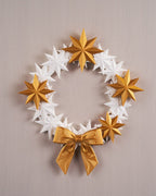 Sternenkranz aus weißen und goldenen 3D-gedruckten Sternen mit goldener Schleife, Frontalansicht an heller Wand
