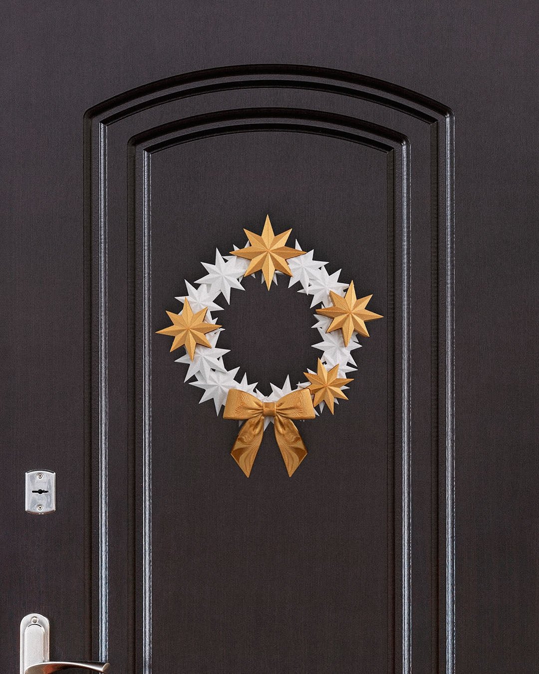 Sternenkranz aus weißen und goldenen 3D-gedruckten Sternen mit goldener Schleife, an dunkler Zimmertür mit Türgriff und Schloss montiert