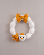 Weihnachtskranz aus weißer Strickoptik mit goldener Schleife, goldenem Stern und Schneemann-Applikation mit Karottennase und goldener Mütze, Frontalansicht an heller Wand