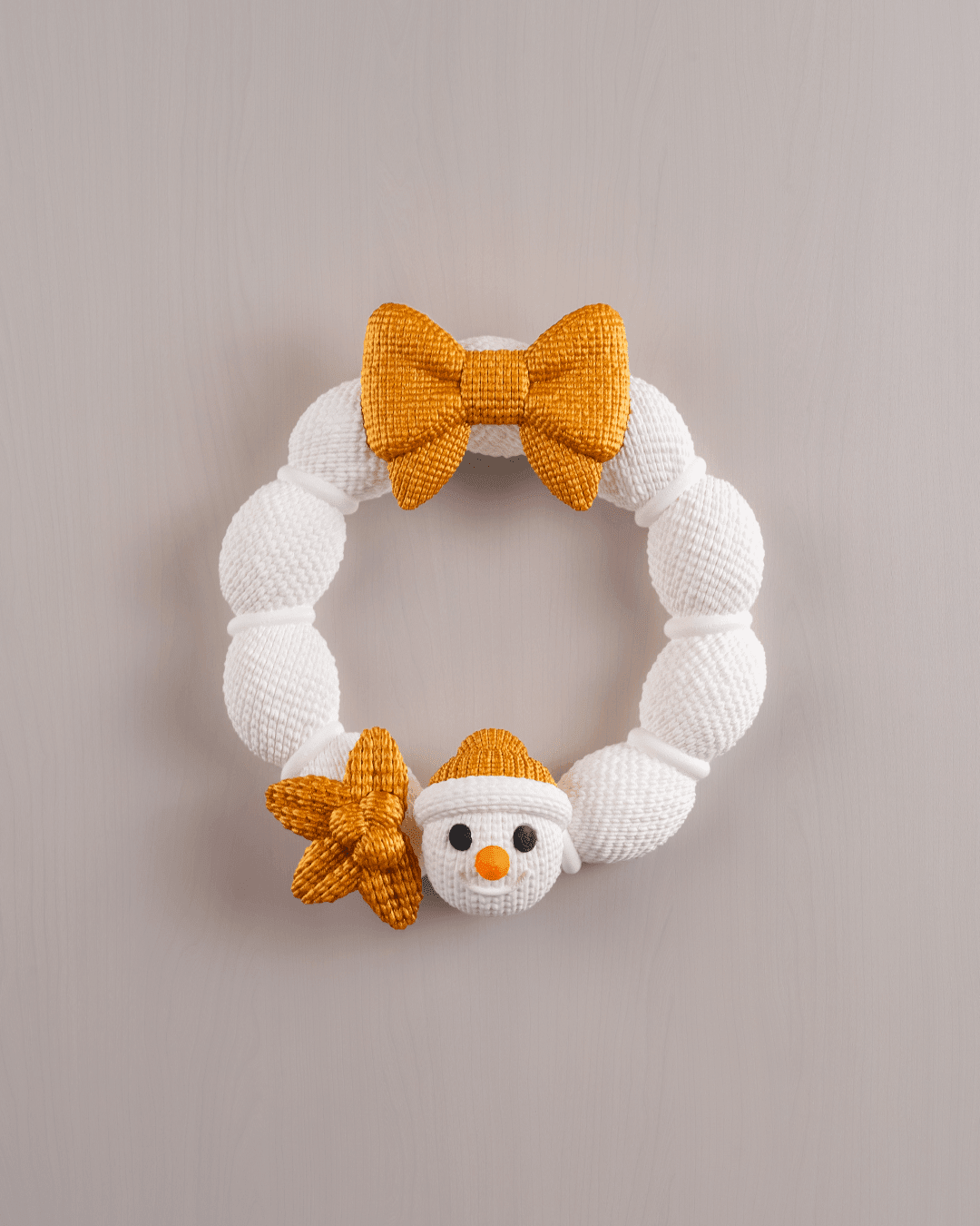Weihnachtskranz aus weißer Strickoptik mit goldener Schleife, goldenem Stern und Schneemann-Applikation mit Karottennase und goldener Mütze, Frontalansicht an heller Wand