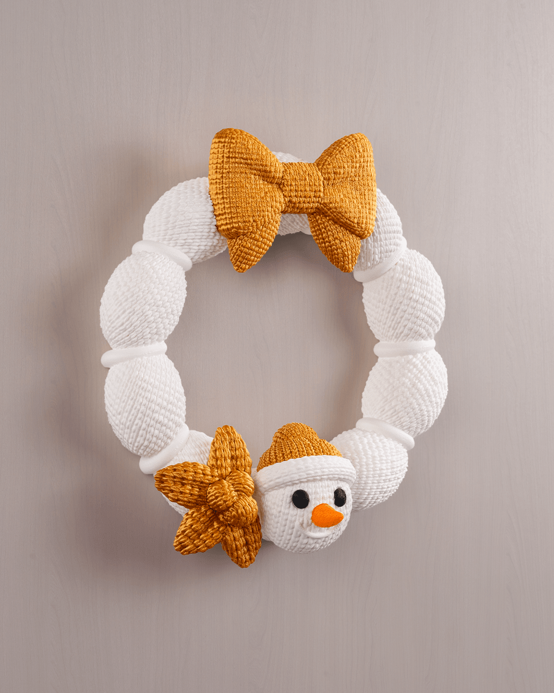 Weihnachtskranz aus weißer Strickoptik mit goldener Schleife und Schneemann-Applikation, Frontalansicht an heller Wand, leicht anderer Bildausschnitt