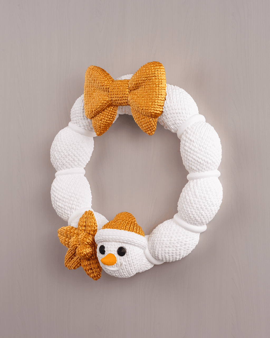 Weihnachtskranz aus weißer Strickoptik mit goldener Schleife und Schneemann-Applikation, Frontalansicht an heller Wand