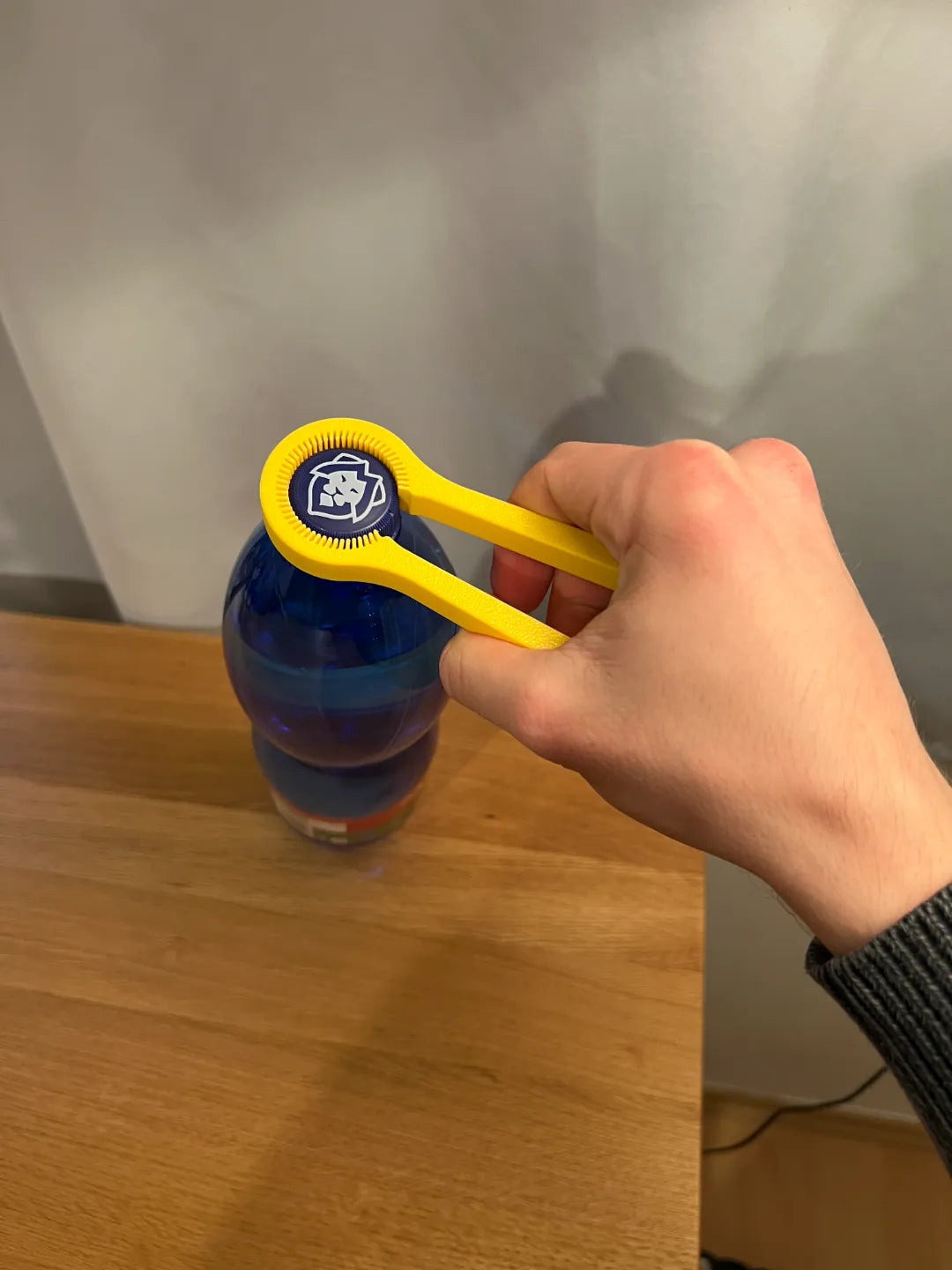 Gelber Flaschenöffner beim Öffnen einer blauen Trinkflasche, Vorderansicht in der Hand gehalten