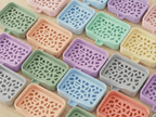 Rasteransicht mehrerer Voronoi-Seifenschalen in verschiedenen Pastellfarben (u.a. Grün, Rosa, Blau, Mint, Orange, Lila, Gelb, Grau, Rot) mit demselben Zellstruktur-Gitter, nebeneinander auf heller Holzfläche.
