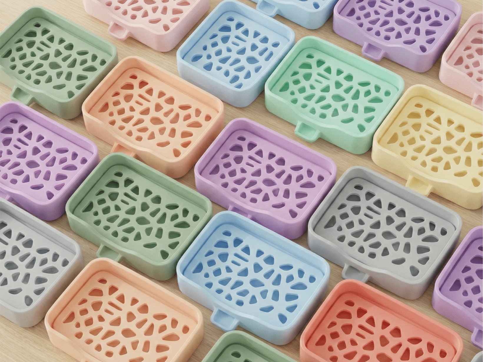 Rasteransicht mehrerer Voronoi-Seifenschalen in verschiedenen Pastellfarben (u.a. Grün, Rosa, Blau, Mint, Orange, Lila, Gelb, Grau, Rot) mit demselben Zellstruktur-Gitter, nebeneinander auf heller Holzfläche.