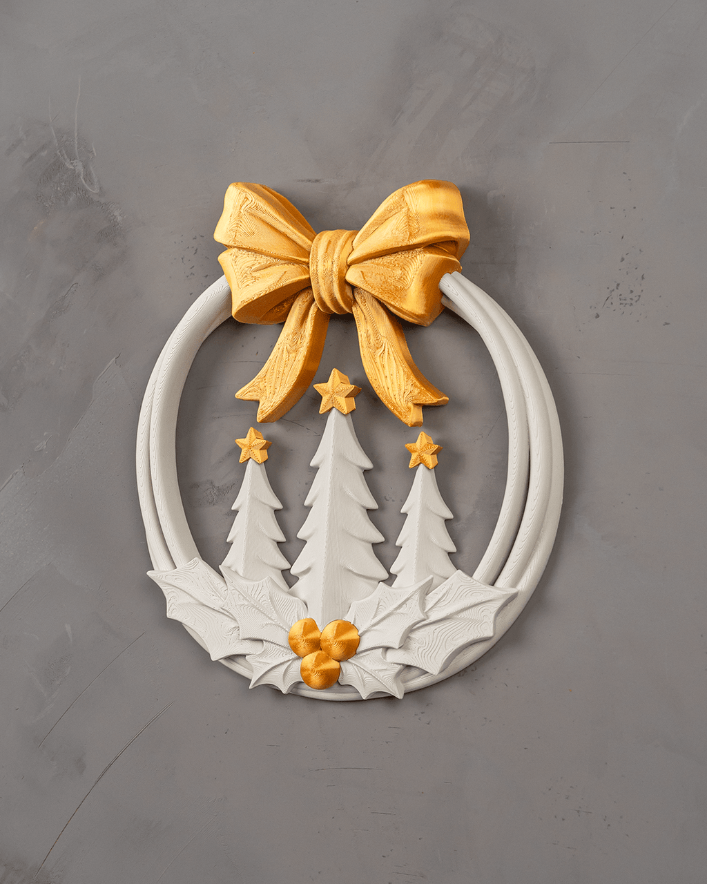 Weihnachtskranz Weiß-Gold frontal an einer grauen Putzwand: goldene Schleife oben, im Ring drei Tannenbäume mit goldenen Sternen, unten Stechpalmenblätter mit drei goldenen Beeren