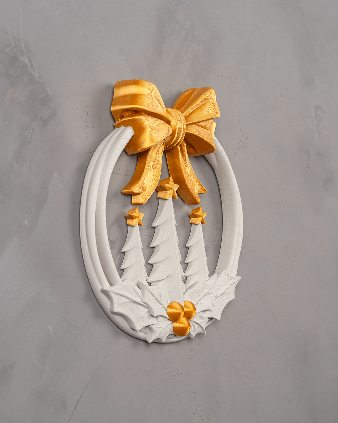 Weihnachtskranz Weiß-Gold in seitlicher Dreiviertelansicht an einer grauen Putzwand, die goldene Schleife steht plastisch vor dem Ring, davor die Tannen und die Stechpalme mit Beeren