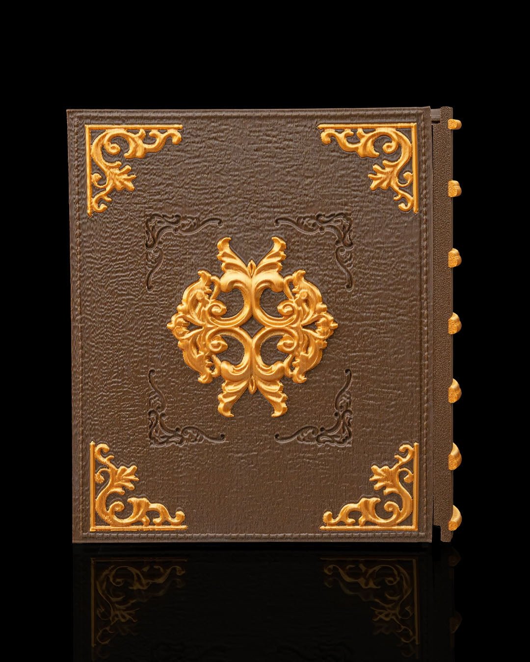 Würfelbox in Buchform, Rückseite mit goldenem Zierornament und verzierten Eckbeschlägen auf braunem Ledercover, kein Totenschädel oder Dolch sichtbar, vor schwarzem Hintergrund