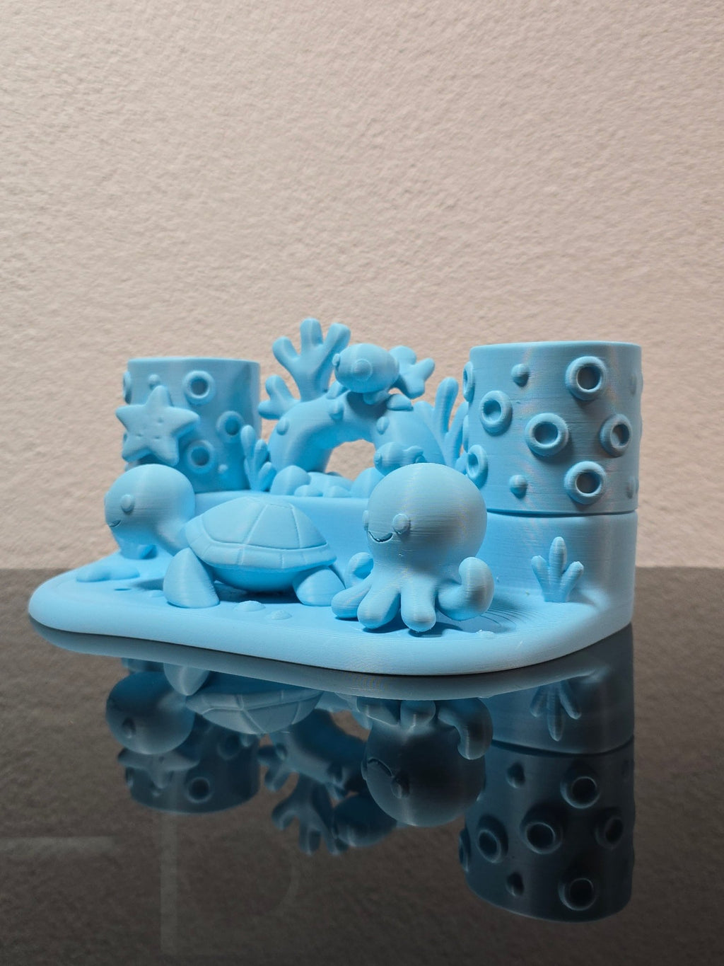 Leerer eisblauer Zahnbürstenhalter mit Schildkröte, Oktopus, Seestern und Korallenbogen aus erhöhtem Blickwinkel, auf dunkler Ablage vor strukturierter Wand