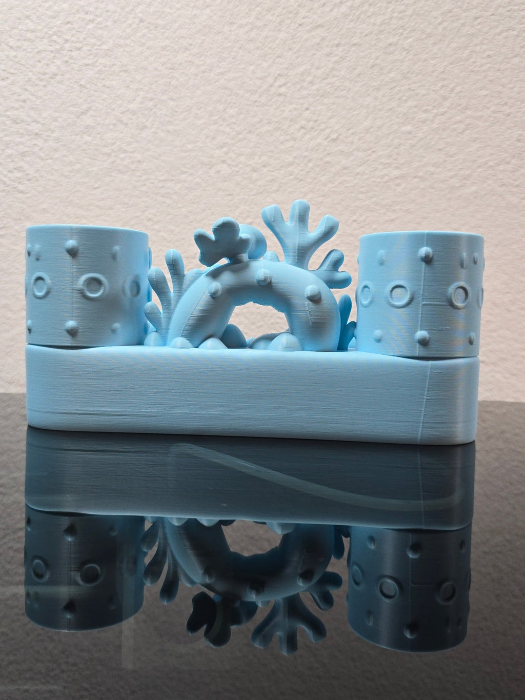 Rückansicht des eisblauen Zahnbürstenhalters mit Korallenbogen, Schildkröte und Oktopus von hinten nicht sichtbar, auf dunkler Ablage vor strukturierter Wand