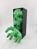 Zombie-Buchstütze mit Totenkopf und greifender Hand aus schwarzer Box, Frontalansicht auf hellem Hintergrund